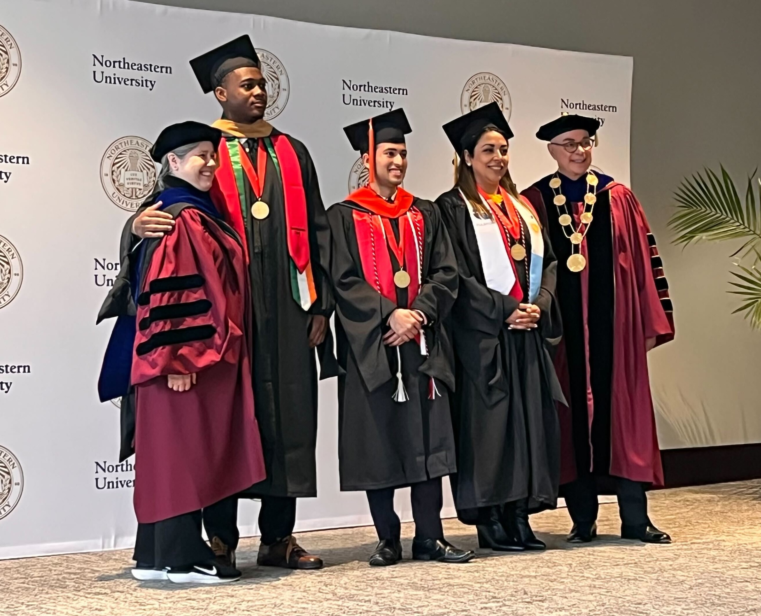 Daniela Gonzalez on stage with Northeastern University Provost Beth Winkelstein and President Joseph E. Aoun, alongside fellow graduate student speakers.